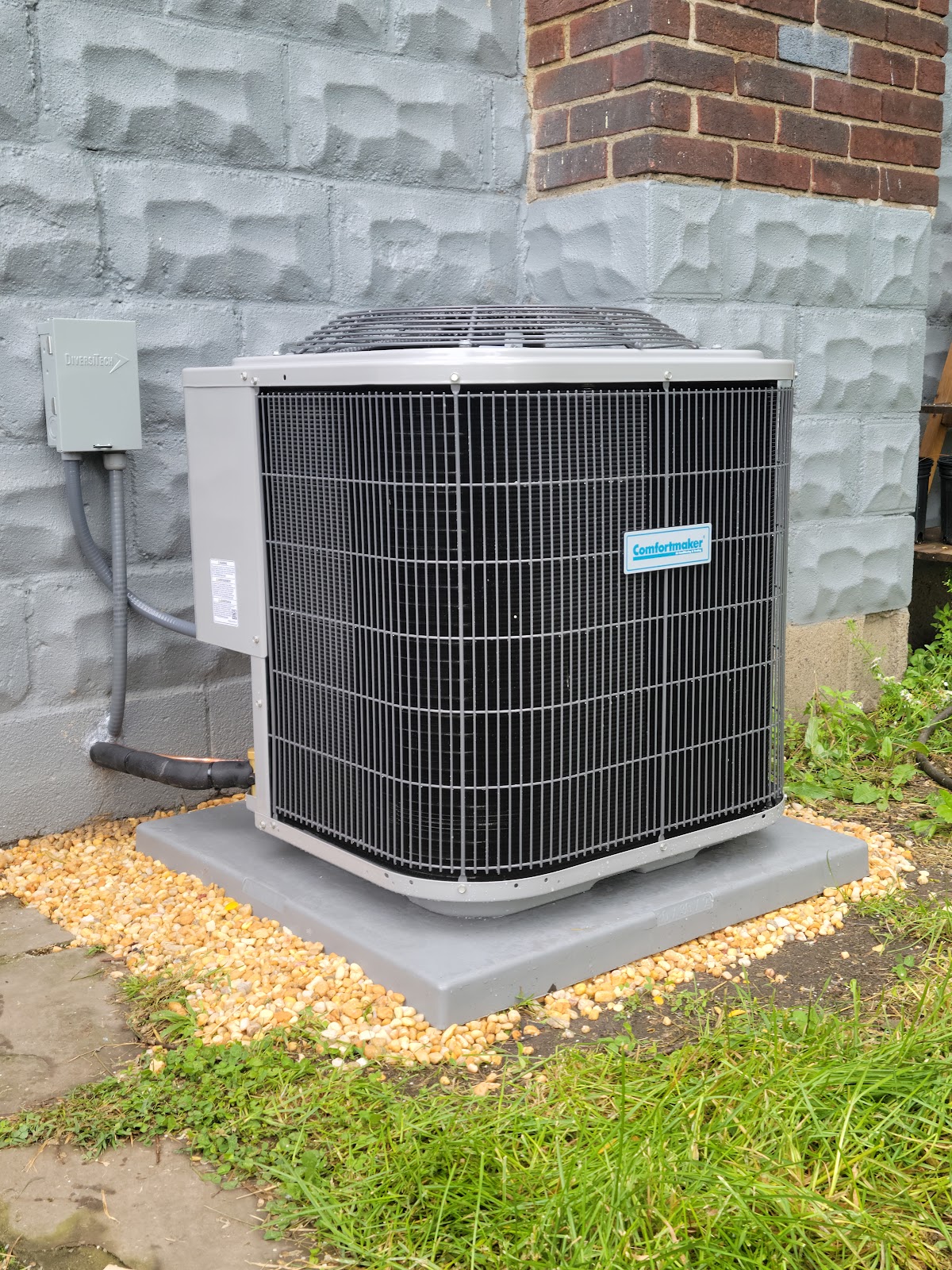 Comfortmaker central air conditioning condenser installed beside a brick and cinderblock home exterior